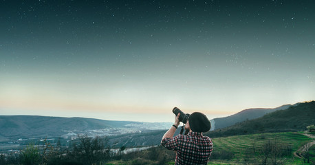 A young man standing atop a mountain at sunset takes pictures of the star sky