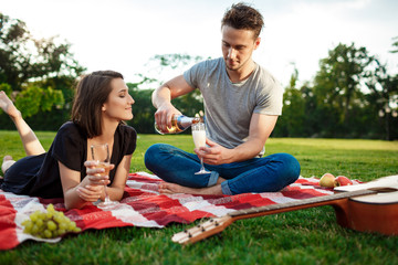 Young beautiful couple smiling, resting on picnic in park.