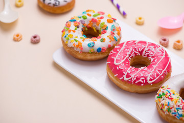 Party. Different colourful sugary round glazed donuts and bottles of drinks on light color background.