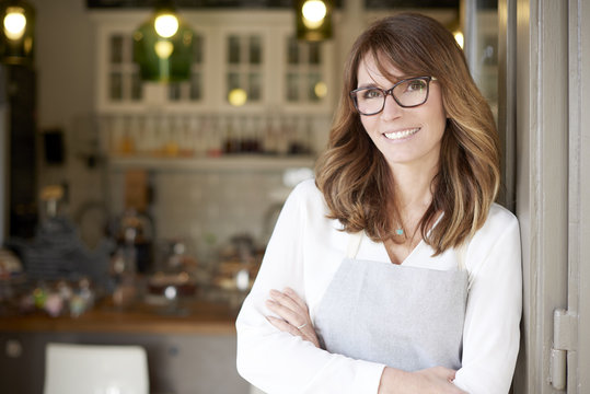 Proud Small Coffee Shop Owner Businesswoman. Shot Of  A Happy Barista Woman Standing At Doorway And Inviting To Her Coffee Shop. Small Business. 