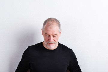 Obraz premium Senior man in black t-shirt, looking down, studio shot.