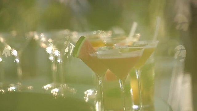 Decorating red cocktail with slice of watermelon. Cosmopolitan and Margarita cocktails on a bar. Party time. Bartender pouring alcohol into beautiful glass outdoors on a sunny, warm summer day.