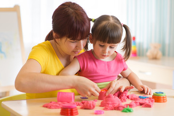 Cute kid and mother playing with sculpting toy at home. Little girl building sandcastle.
