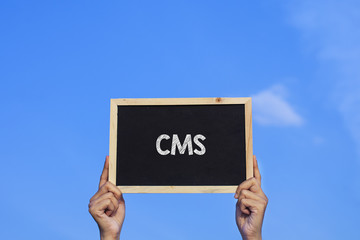 CMS/ Man holding small blackboard on blue sky background.