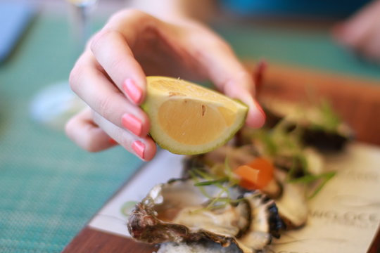 Main de femme au ongles vernis pressant un citron sur une huîtres au restaurant