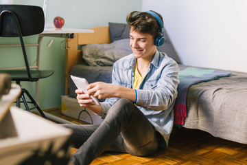 Teenage boy using tablet and listening music in his room