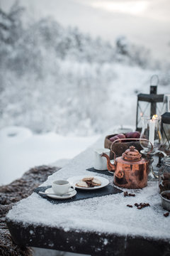 Coffee, biscuits, copper colour tea pot on snow covered picnic bench 