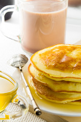 Glass mug with cocoa, silver spoon, honey and pancakes