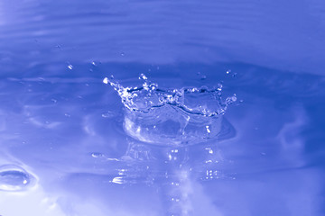 Water splash in dark blue color with a drop of water flying from above