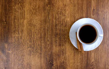 A cup of coffee and cinnamon on a wooden table. View from above.