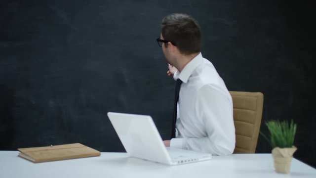 Businessman with laptop moving his hand as if underlining a word on chalkboard