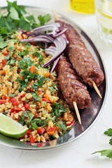 Bulgur salad with  meat kebab of minced beef or lamb with vegetables and herbs .  Top view