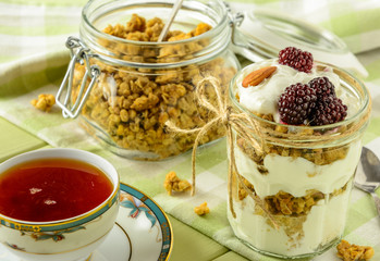 Healthy breakfast ingredients. Homemade granola with yogurt in open glass jar and cup of tea. The food is rich in useful carbohydrates, vitamins and nutrients that are essential for health. 