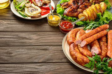 Dinner table with variety food, fried chicken wings, sausages, grilled vegetables in a pan, salad and  lager beer on dark wooden table.  Copy space. Indoor food Concept. Rustic style.