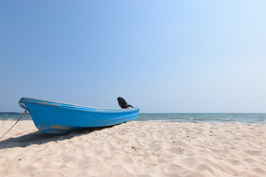 Colorful blue fishing boat with outboard motor on white sandy beach.