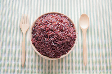 Purple rice in a Wooden bowls, wooden spoons and wooden forks. Organic rice in a wooden bowl with spoon and fork on a green mat.