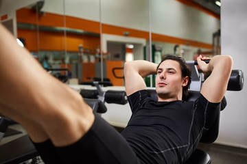 Fototapeta na wymiar Athletic man in the black sportwear doing exercises on legs in gym.
