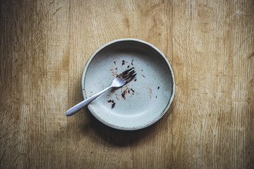 Empty plate and fork of dessert after meal on wooden table