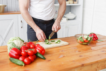 Middle-aged athlete, cuts vegetables salad of cucumber and tomato. Vegetarian food