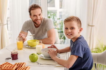 Obraz na płótnie Canvas Joyful son eating cereals with his daddy