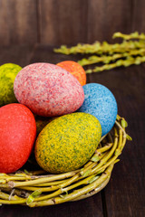 Colorful painted eggs in a nest of twigs of willow on a dark wooden background. Traditionally for Easter. Vertical view.