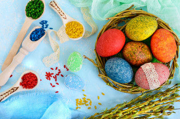 Fototapeta na wymiar Colorful painted eggs in a nest of twigs of willow on a light background and multicolored rice for decorative painting. Traditionally for Easter. The top view