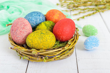 Colorful painted eggs in a nest of twigs of willow on a light background. Traditionally for Easter.