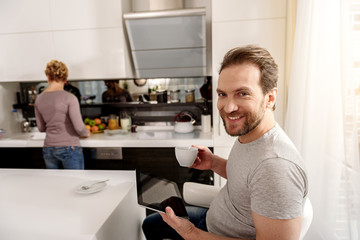 Cheerful husband waiting for breakfast in kitchen