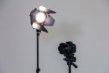 Digital SLR camera and a spotlight with a Fresnel lens on a gray background. Shooting in the interior. Equipment for the production of films.