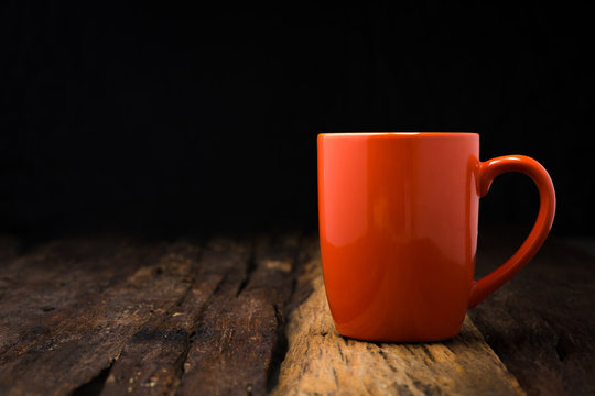 Orange ceramic empty mug on old wooden table top with copy space warm tone processed