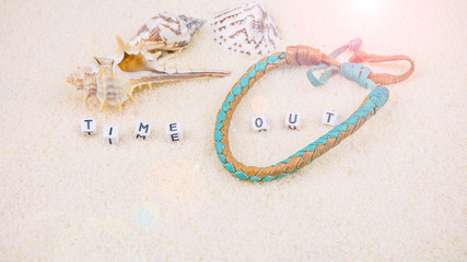 Fototapeta na wymiar Time out letters in front of sea shells and coloured wristbandon on sandy beach