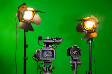 A video camera and a spotlight with a Fresnel lens on a green background. Filming in the interior....