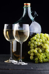 Bottle and glass of white wine, grape on wooden table