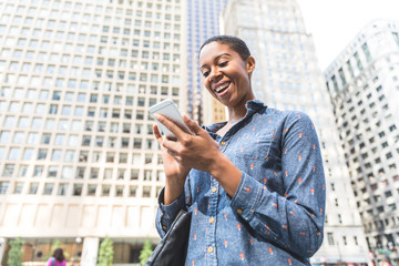 Black woman typing on the phone in the city