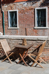 Fototapeta na wymiar Wooden table and chairs of sidewalk cafe in Venice, Italy, with brick wall in the background, no people