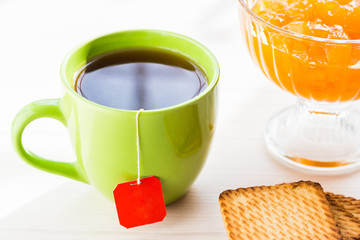 Black tea in green cup with cookies and apricot jam
