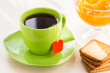 Black tea in green cup with cookies and apricot jam