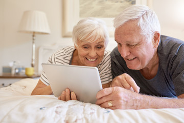 Smiling senior couple using a digital tablet together in bed