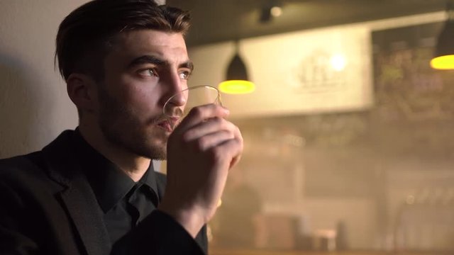 The close-up side portrait of the upset mab in the black suit drinking beer and looking somewhere esle in the bar.