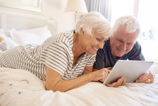 Happy senior couple lying in bed using a digital tablet