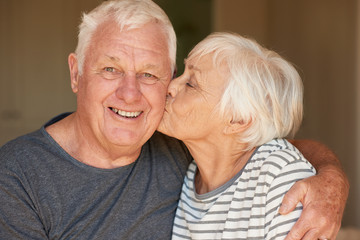 Senior woman kissing her smiling husband in the morning