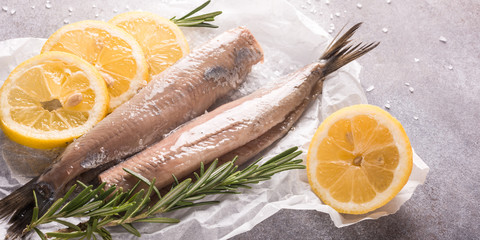 Freshly salted herring with salt, lemon ans rosemary on gray background. Traditional Dutch...