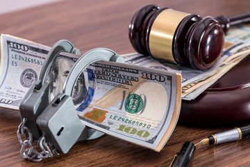 Wooden Gavel, handcuffs and dollar bills on desk.