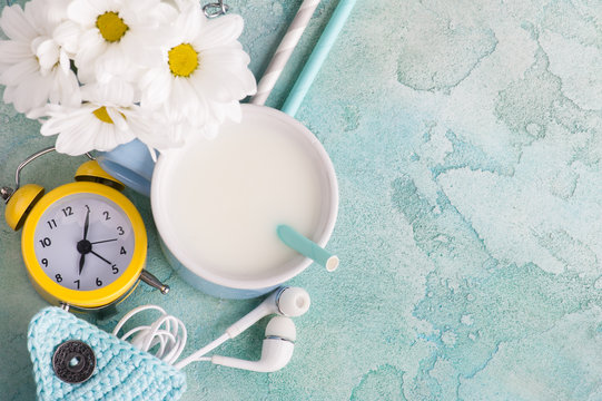 A mug of milk with straw, headphones and clock