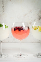 Selection of three kinds of gin tonic: with blackberries, with lime, with mint leaves. In glasses on a white background. Copy space 