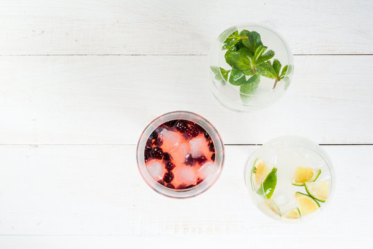Selection of three kinds of gin tonic: with blackberries, with lime, with mint leaves. In glasses on a white background. Copy space top view