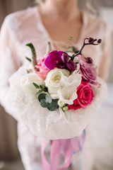 Beautiful girl in tender lacy dress with bouquet flowers peonies in hands standing against floral background in flower shop. Joyful asian female florist. Shy fashion model looking down and smiling.
