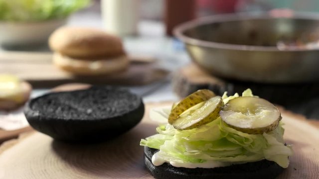 Black burger bun and lettuce. Slices of pickled cucumber.