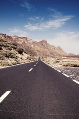 long straight road through desert landscape with mountains in background under blue sky