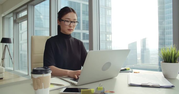young successful Asian business girl in a modern office skyscraper, working using laptop